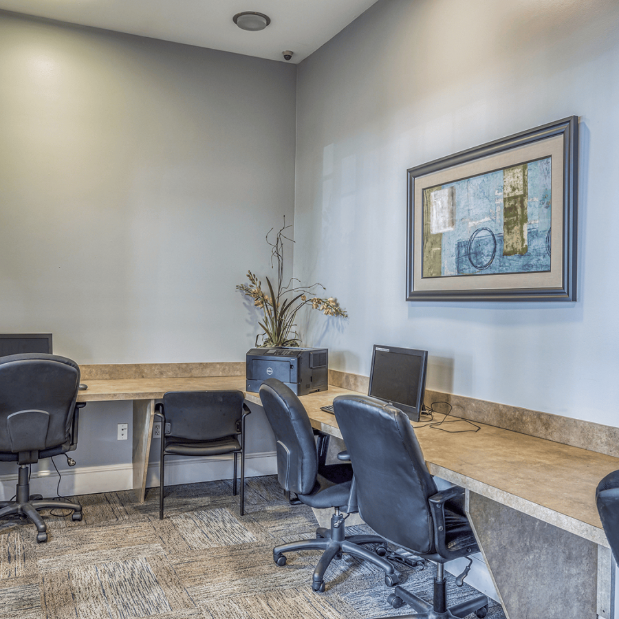 Small office with four black chairs, three computers on a counter, a window, and a painting on the wall.