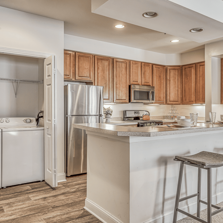 Modern kitchen with stainless steel appliances, wood cabinets, and laundry area with washer and dryer on the left.